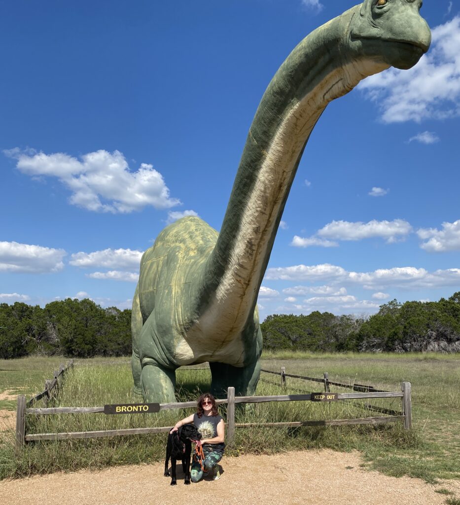 Toni and her dog Clyde in front of Bronto Statue in Glen Rose Texas